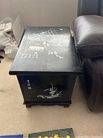 Photo showing one black side table with mother of pearl inlay floral and bird designs on top and side near leather chair.