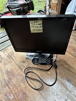 Front view of ViewSonic LCD TV on a wooden floor with remote control and power cord placed in front. Sticky note on screen reads dimensions and not tested.
