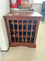 Front view of wooden wine rack filled with wine bottles behind vertical wooden bars showing condition and design.