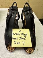 Front and top views of the pair of BCBG Girls women's black slingback high heels with leopard print details and size 7 indicated on a note.
