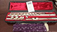 Yamaha flute disassembled into three parts inside black hard case with red velvet lining, along with purple cloth.