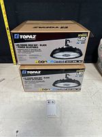 Two boxed Topaz LED Round High Bay lights stacked, showing product branding and packaging.