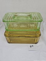 Stacked view of two glass refrigerator dishes with lids, green oblong on top of amber square dish showing ribbed patterns