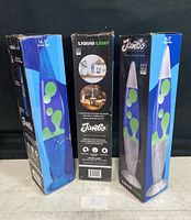 Three boxes of Jambo Liquid Wax Lava Lamps standing upright. Boxes show some wear. Lamps are new in box and untested.