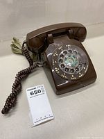 Front and top view of brown rotary phone showing rotary dial and handset on a flat surface.