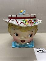 Front view showing the girl's face, hat with flower decoration, and blue bow