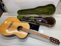 Violin in open case next to acoustic guitar and black cushion on table, view from above.
