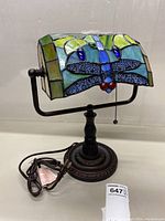 Side view of Tiffany style dragonfly desk lamp showing detailed stained glass shade and metal base with electrical cord.