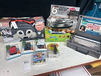 Wide view of raccoon bag, remote control tank, Lite Brite box, phone cases, patch kit on table