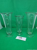 Full view of the three vintage etched glass science beakers varying in size including one with a crack on the base.