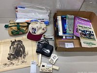 Overview photo of the memorabilia lot showing cap, cooler bag, folded towel/banner, canvas tote bag, binoculars, slides, and box of books/programs.