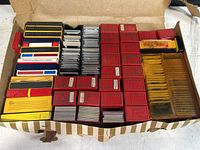 Top-down view of a variety of vintage slide boxes including red Pavelle Color plastic boxes and other colored boxes, all containing photographic slides.