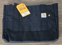 Front view of black Carhartt tote bag showing the logo patch, sturdy construction, and tag indicating built-to-last qualities.
