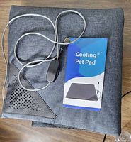 Dark gray cooling pet pad folded with attached USB power cable and cooling pet pad instruction booklet.