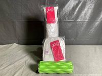 Photo shows green textured foam roller by Gaiam with a white Jogi exfoliating bath strap and pad in packaging