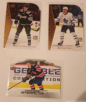 Front view of three rookie hockey cards showing Luke Hughes in black New Jersey Devils uniform, Matthew Knies in white Toronto Maple Leafs uniform, and Connor Bedard retrospective card in red and blue Regina Pats uniform.