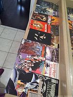 Top view of stacked comics laid out in cardboard box showing various titles with colorful, graphic covers depicting horror and sci-fi scenes. Includes Aliens, Shadow Hawk, and other horror themes.