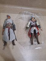 Two Assassin's Creed figures side by side showing outfit and size