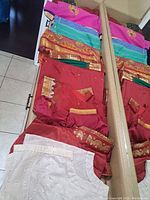 Photo showing folded Indian sarees with bright colors including pink, turquoise, red, and purple, and some gold embroidered detailing.