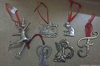 Six metal hanging ornaments including reindeer, sleigh, angels, girl with candle, and initial F, all with red ribbons for hanging.