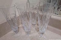 Photo of six tall crystal flute glasses with pinwheel cut pattern, arranged on a counter.