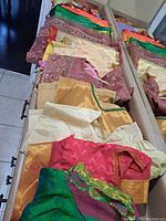 Folded Indian sarees laid out with matching tops on a dresser, showing color and fabric detail