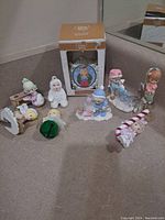 Photo showing all nine Christmas ornaments arranged on a surface including one boxed Precious Moments item and various winter-themed figurines.