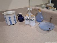 Hexagonal ceramic planter with blue leaf pattern, dark blue small pitcher, white porcelain salt and pepper shakers with floral details and gold tops, blue opaline glass perfume atomizer with bulb, frosted blue glass dish with two brass handles.