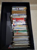 Photo of a stack of assorted sports cards in a black box, showing edges and multiple card backs and fronts.