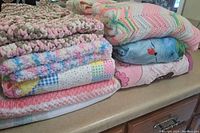 Stack of six baby blankets and quilts showing textures and colors, highlighting crocheted and patchwork designs