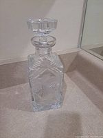 Front view of clear crystal decanter showing geometric cut and floral design with stopper on top.