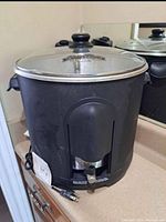 Front view of black electric turkey fryer with glass lid, showing spigot and power cord.