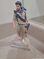 Front view of Nathan Drake figure on a stone-textured base with Uncharted 3 logo.