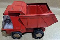 Side view of the red vintage Buddy L toy dump truck showing the movable dump bed and metal construction
