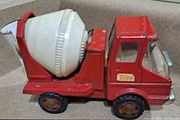 Left side view of the vintage Cragstan red metal toy cement mixer truck showing the white plastic rotating drum and cabin side details