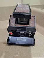 Front view of vintage Polaroid SX-70 Land Camera Model 3 showing textured brown panels and lens area.
