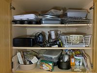 Full view of three shelves containing metal pans, racks, mixers, measuring cups, baking supplies and miscellaneous smaller items.