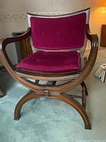 Front view showing the curved X design wood frame, tufted red velvet seat and back cushions, and cane seat base.