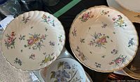 Two large scalloped white bowls with multicolor floral designs and gold trim on their rims.