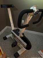 Full view of white CCM 977 stationary exercise bike with black seat and handlebars on carpeted floor.