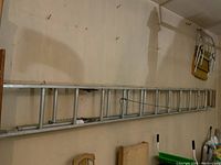 Full view of aluminum extension ladder hung horizontally on wall in garage.