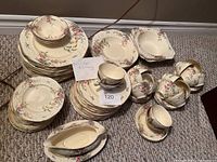 Full set of floral china arranged on floor showing multiple plates, cups, saucers, bowls and 2 gravy boats