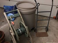 Photo showing Rubbermaid garbage can behind the Ames green hose wheel and the black metal dolly with wooden base