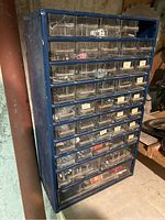 Blue plastic storage unit with multiple clear plastic drawers filled with assorted nails and screws. Drawers are labeled or partially filled.