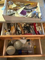 Overview of two drawers showing kitchen tools including metal whisks, can openers, kitchen scissors, bowls, and plastic containers.