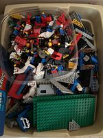 Two bins showing assorted Lego parts including minifigures, horses, shields and base plates