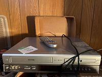 Front view of silver Toshiba VHS/DVD combo player with remote on top
