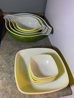 Stacked set of four nested green to yellow gradient mixing bowls and square casserole with four small matching serving bowls stacked inside.