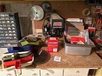 Wide view of Craftsman radial saw on workbench with various saw blades, dustpans, sanding supplies, and disposable mask box in foreground.