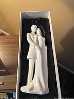 Front view of white Royal Doulton figurine of a bride and groom in an embrace inside original box with black fabric lining.